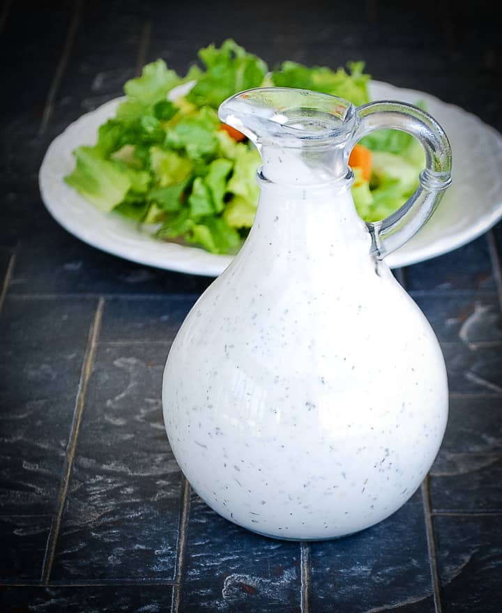 bottle of homemade ranch dressing with a plate of salad in the background
