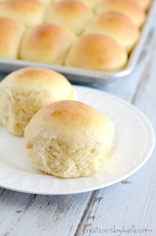 white rolls on a plate with a pan of rolls in the background