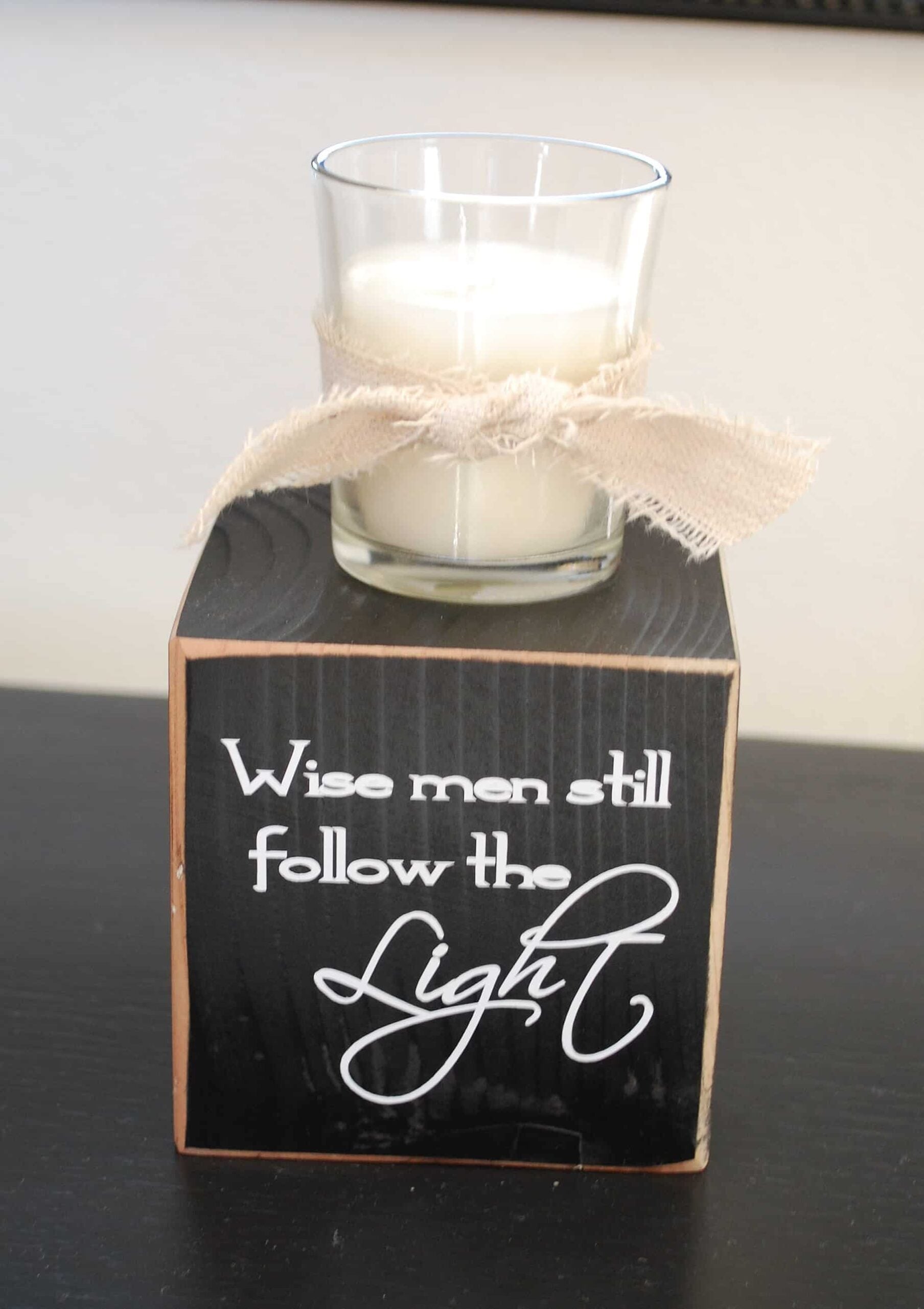 Wise Men Still Follow The Light Candle Block A black painted wood block lettered Wise men still follow the Light with a glass votive candle and a frayed canvas bow on top