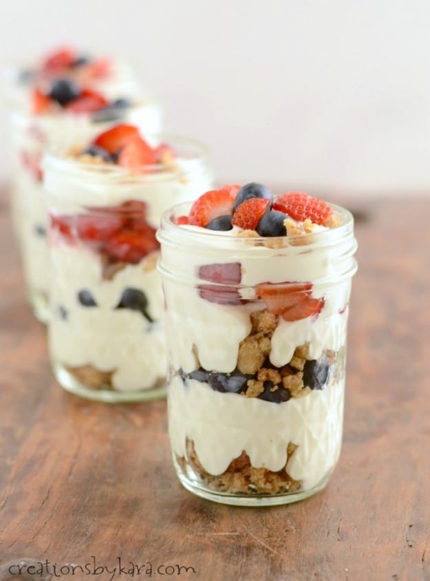 mason jars filled with cheesecake filling, berries, and crumb topping
