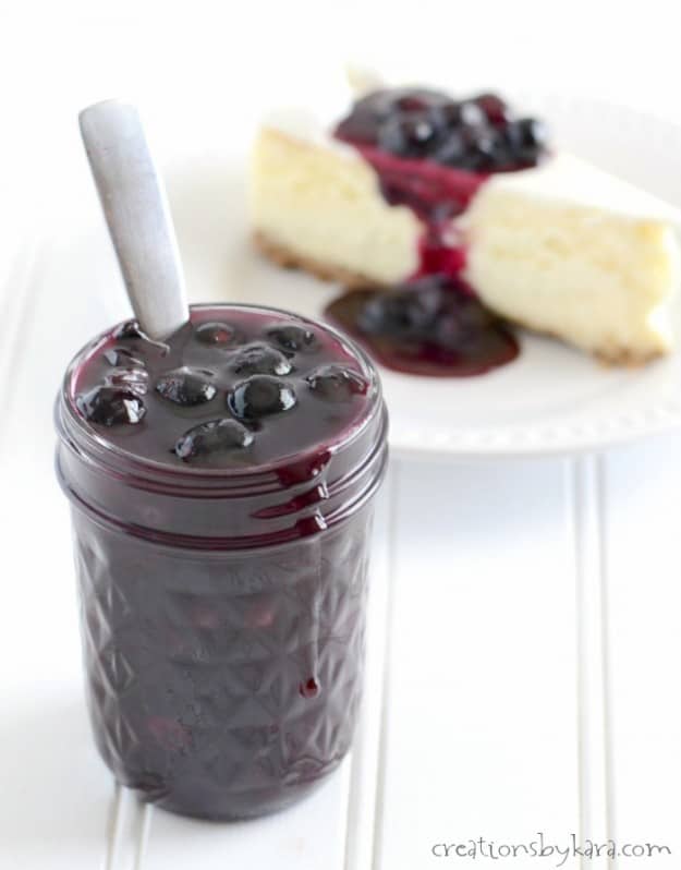 jar of Homemade Blueberry Sauce in front of a slice of cheesecake