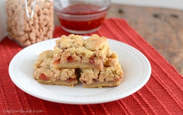 stack of peanut butter jam bars on a plate with jam in the background