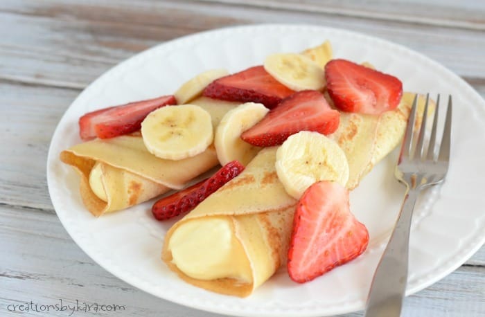 plate of dessert crepes with cream filling, strawberries, and sliced bananas