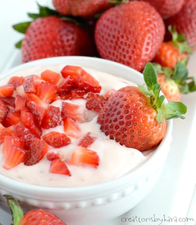 white bowl of strawberry cheesecake dip with a fresh strawberry