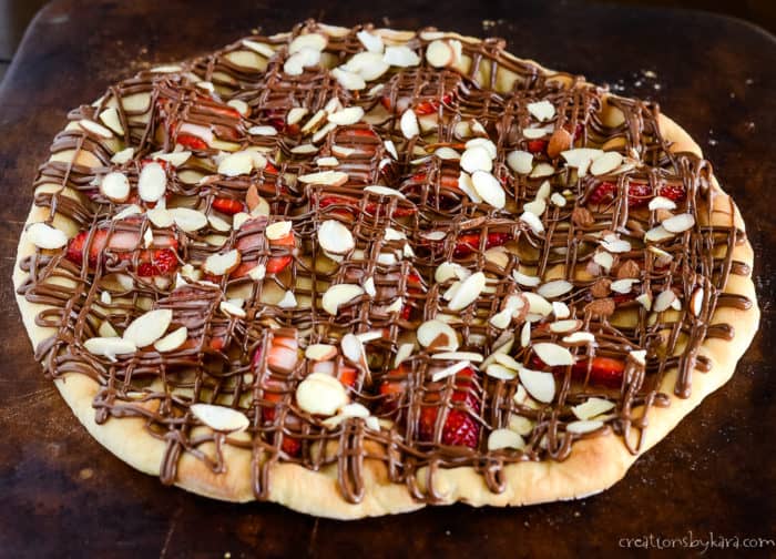 dessert pizza with strawberries, bananas, sliced almonds, and a drizzle of Nutella