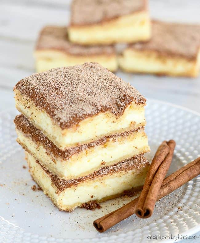 stack of churro cheesecake bars on a white plate with cinnamon sticks