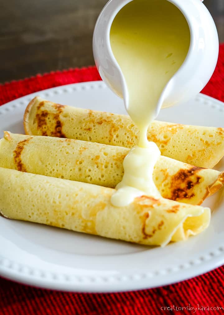 vanilla custard sauce being poured over crepes