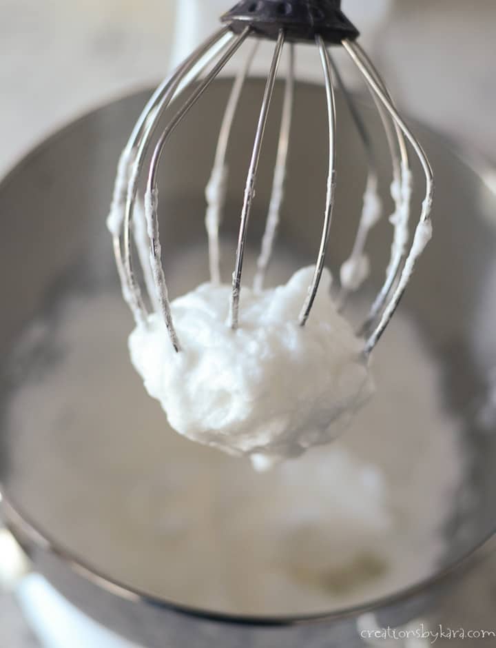 beaten egg whites on a kitchenaid whisk over a bowl of egg whites