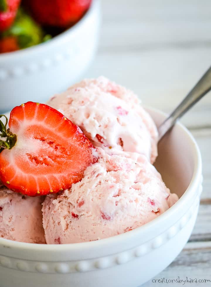 close up shot of strawberry ice cream in a bowl with a fresh strawberry