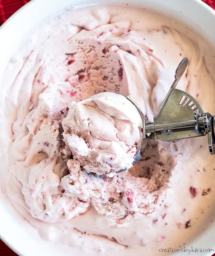 bowl of strawberry ice cream with a spoon and a bowl of strawberries in the background