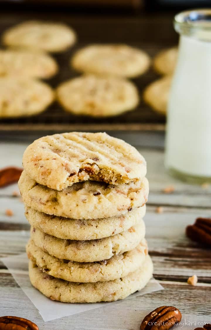 pecan sandies cookies in a stack with a glass of milk and cooling rack in the background