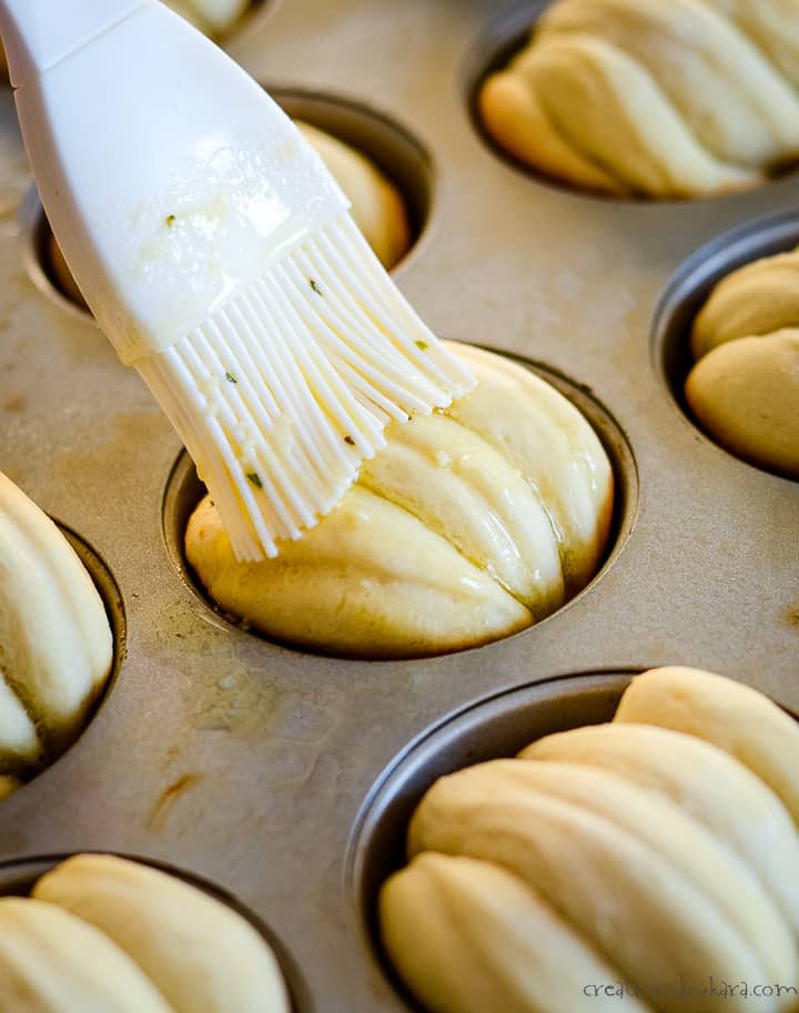 brushing garlic butter on pan of hot rolls