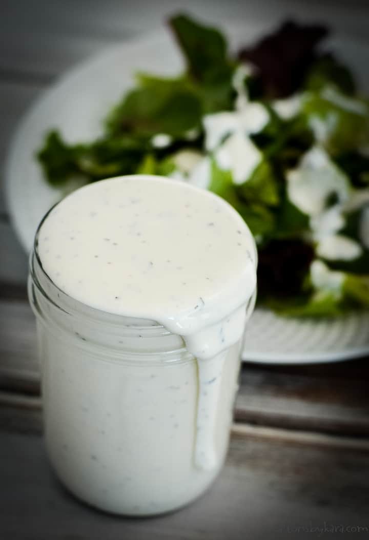 mason jar of keto ranch dressing in front of a plate of salad