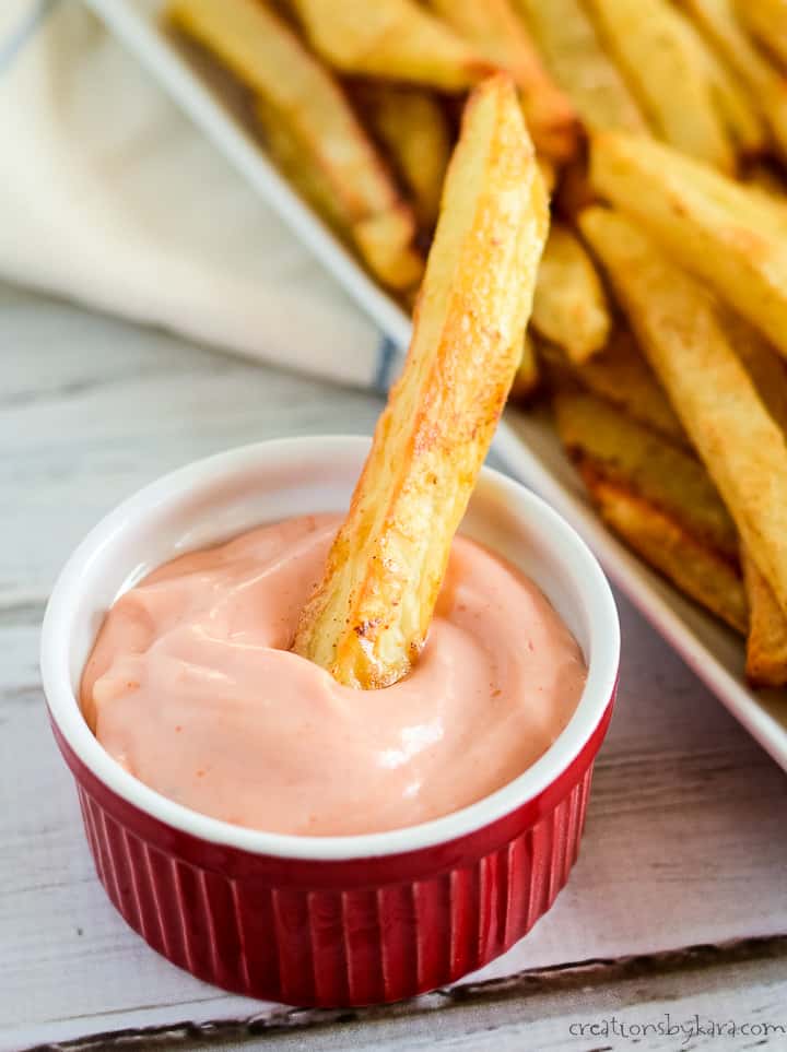 crispy oven baked fries, one being dipped in fry sauce