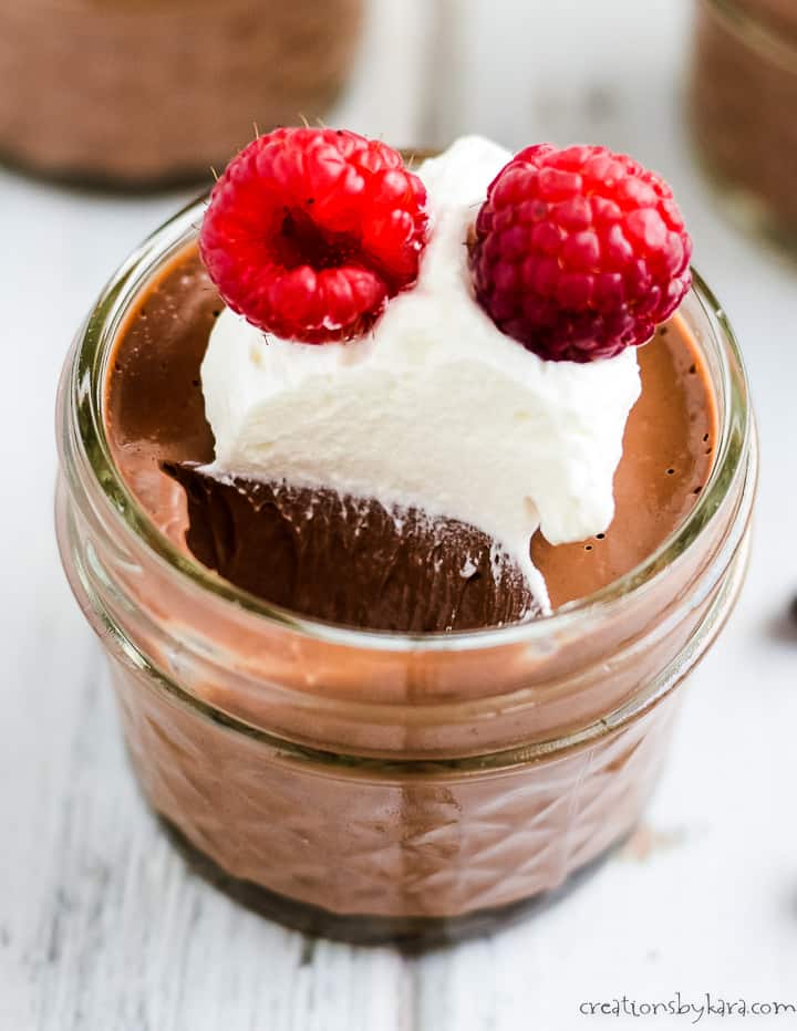 close up of mini mason jar filled with chocolate mousse and garnished with whipped cream and berries