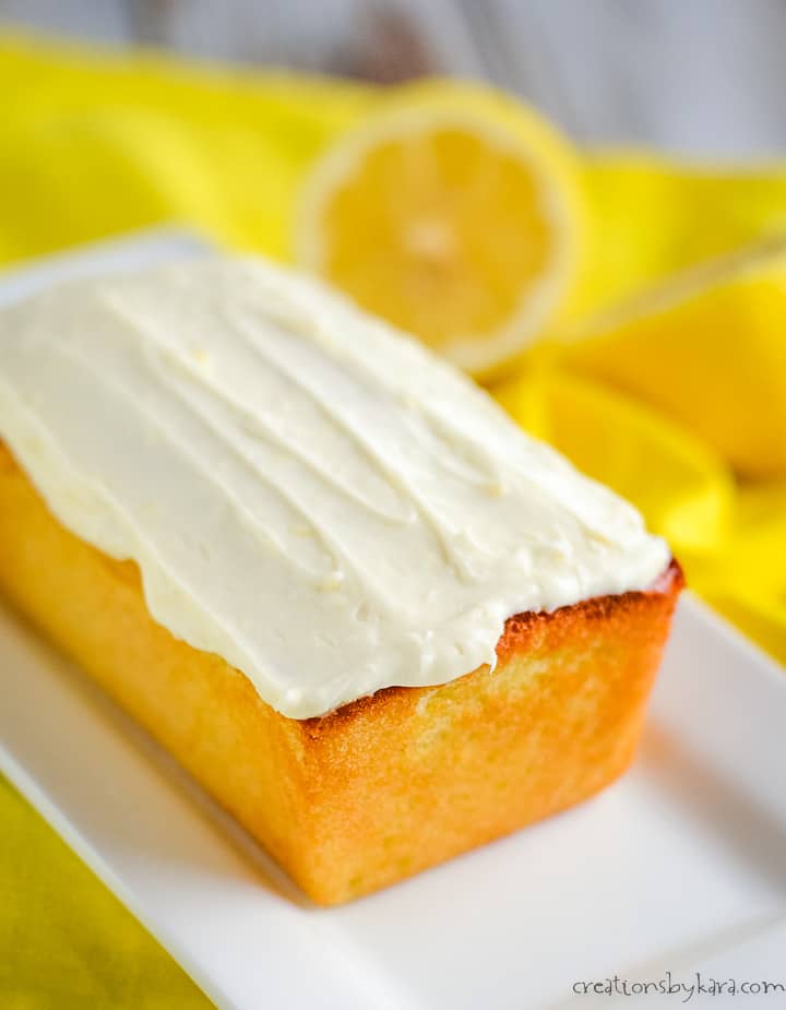 frosted lemon keto cake on a white serving tray with lemons in the background