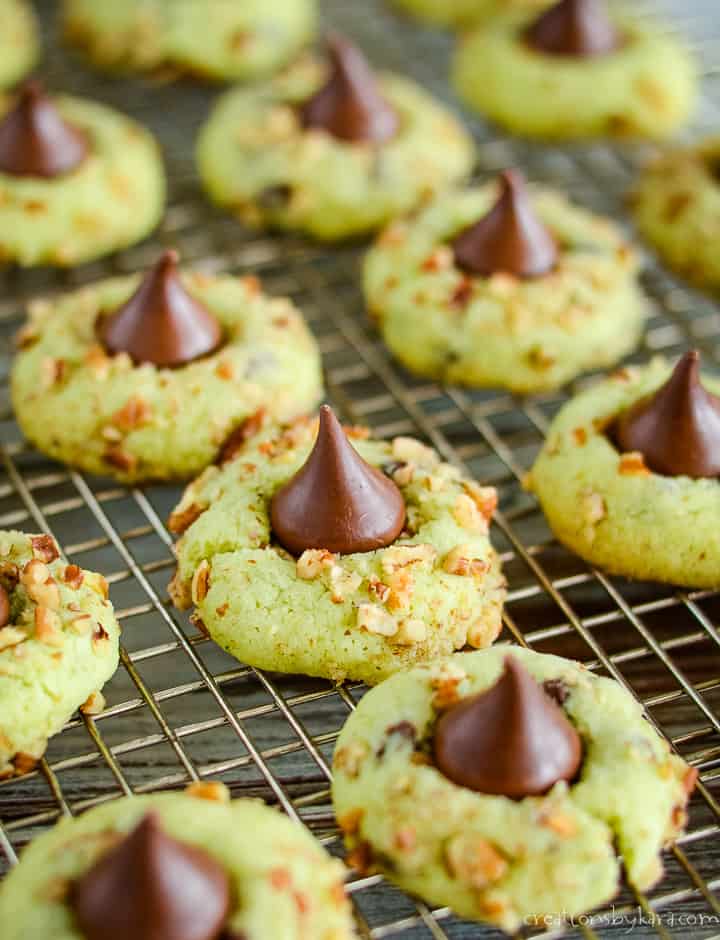 Pistachio Kiss Pudding Cookies are a fun twist on classic blossom cookies. People can't resist a cookie topped with a chocolate kiss! #kisscookies #pistachiokisscookies #christmascookies pistachio kiss pudding cookies on a cooling rack