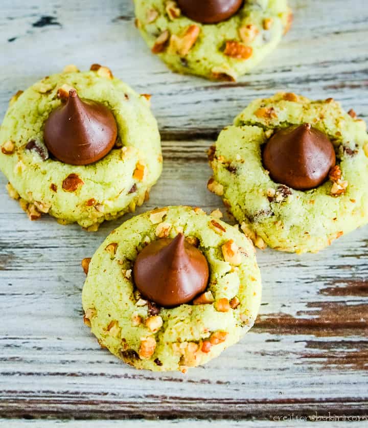 These Pistachio Kiss Pudding Cookies are just perfect for Christmas! A fun green Christmas cookie rolled in nuts and topped with a Hershey kiss. #christmascookies #kisscookies #puddingcookies #pistachiocookies -creationsbykara.com overhead shot of pistachio cookies