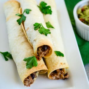 ground beef taquitos on a tray sprinkled with parsley