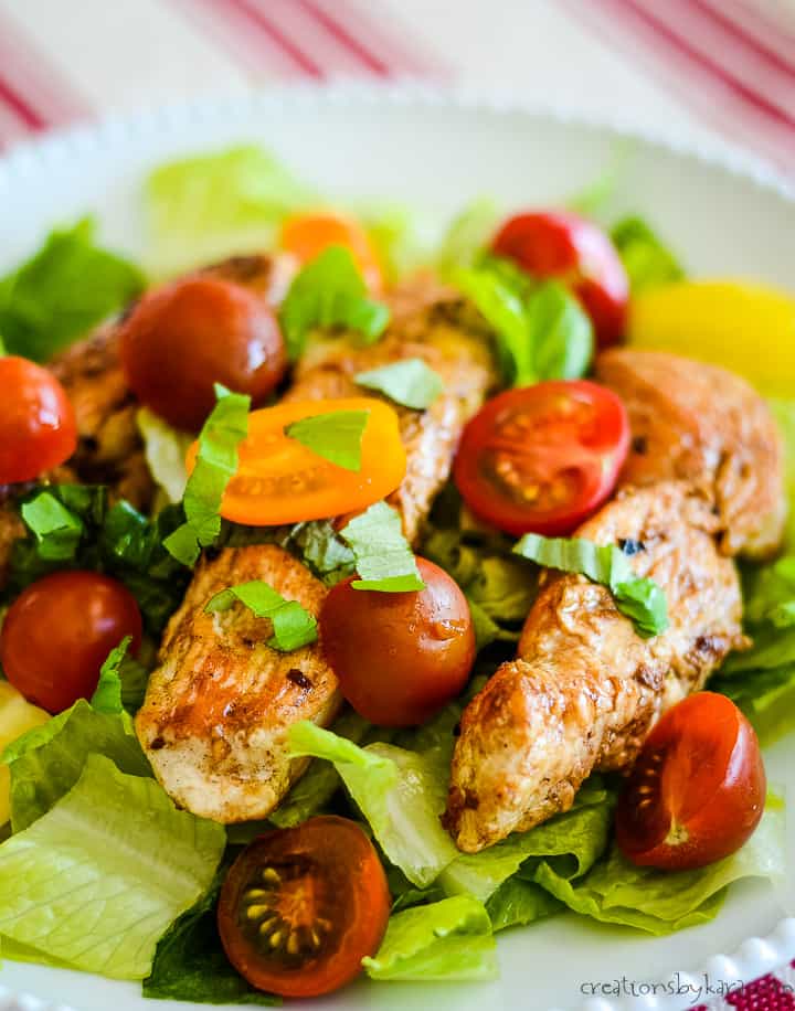 balsamic glazed chicken on top of salad greens topped with halved tomatoes and fresh basil