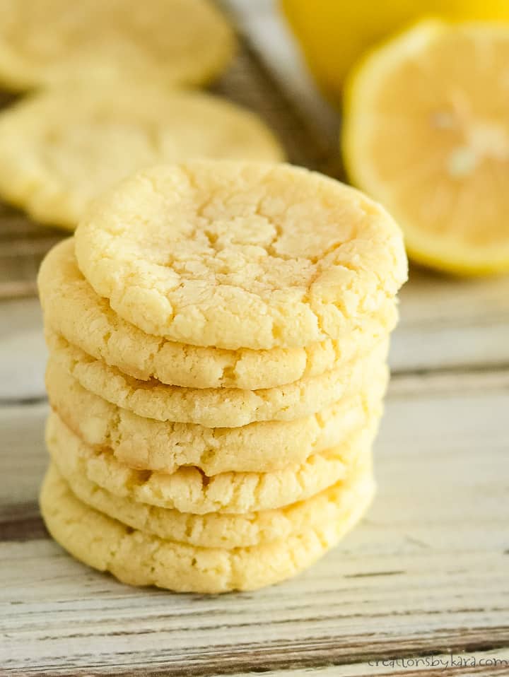 stack of lemon crinkle cookies with a cookie sheet of cookies in the background