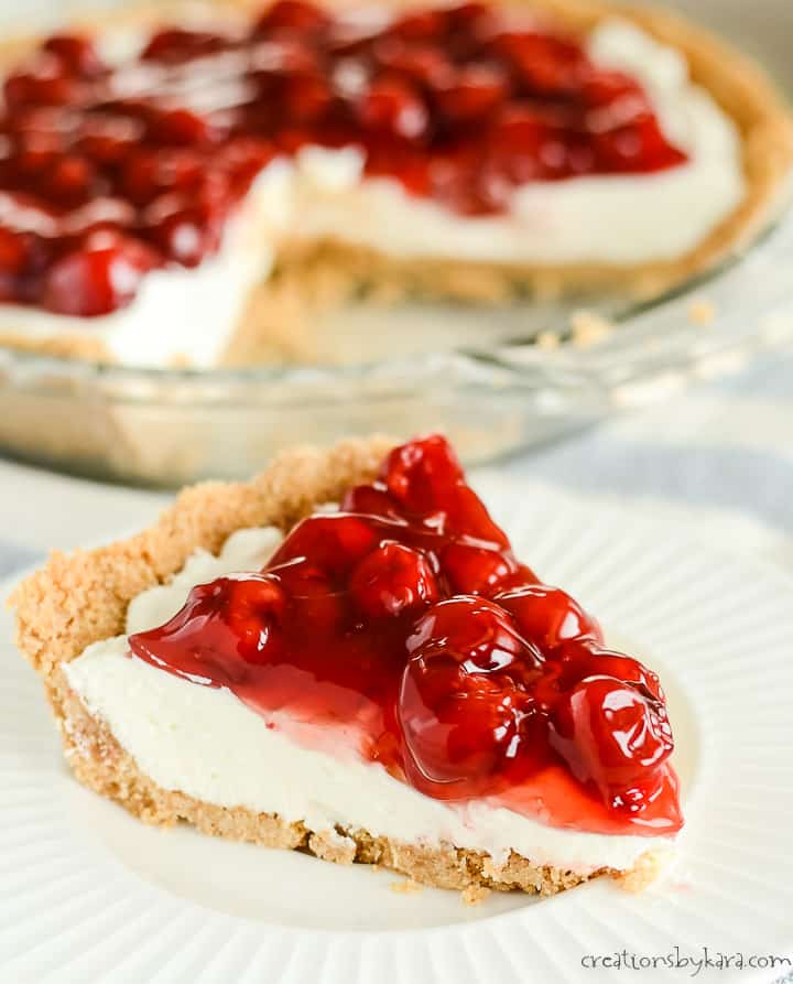 slice of no bake cherry cheesecake on a plate with a pan of cheesecake in the background