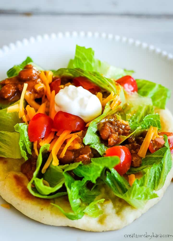 fry bread taco on a plate with lettuce, cheese, tomatoes, chili, and sour cream