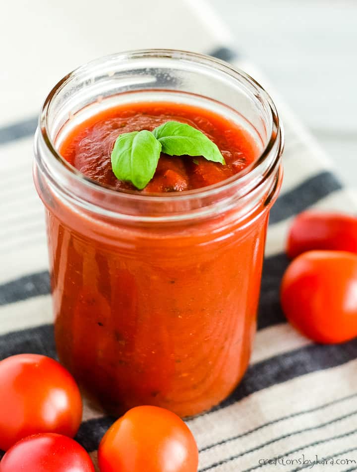 jar of homemade pizza sauce on a dish towel with grape tomatoes