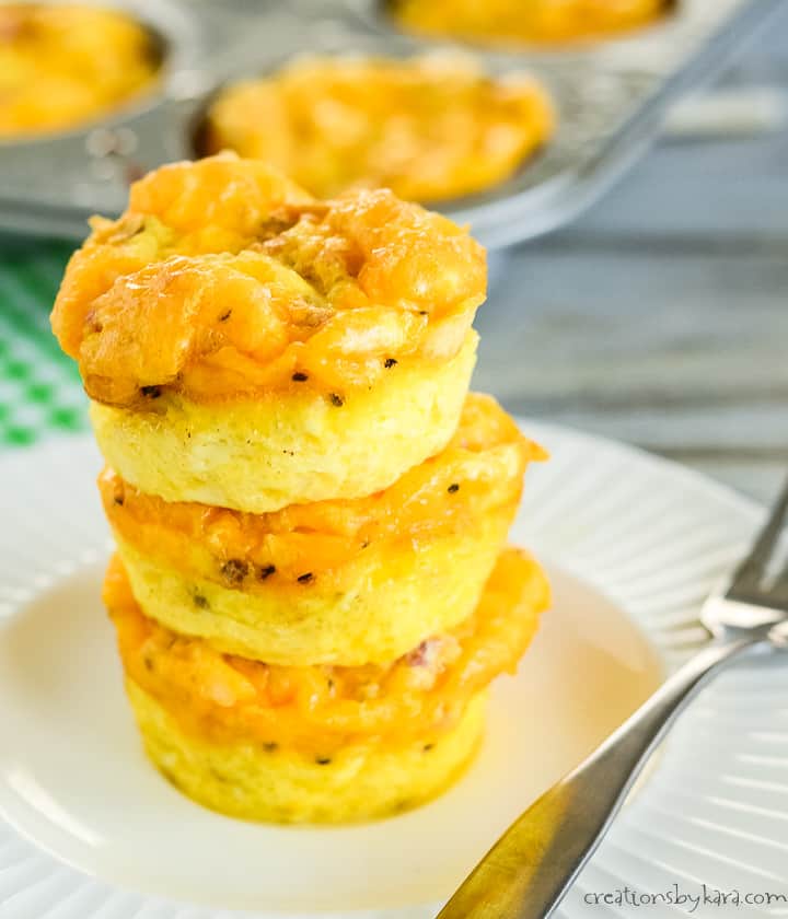 plate with a stack of egg muffin cups with ham and cheese, muffin tin in the background