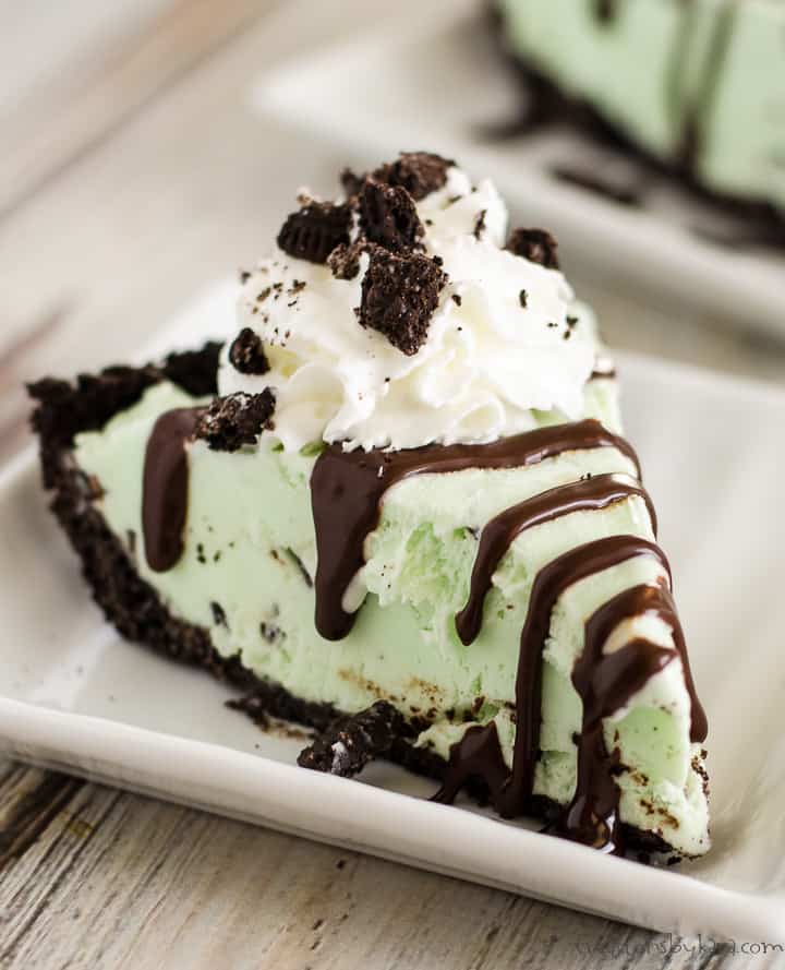 slice of grasshopper ice cream pie on a white plate with hot fudge, whipped cream, and crushed oreos