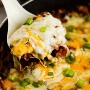 mexican casserole topped with melted cheese being scooped out of a skillet