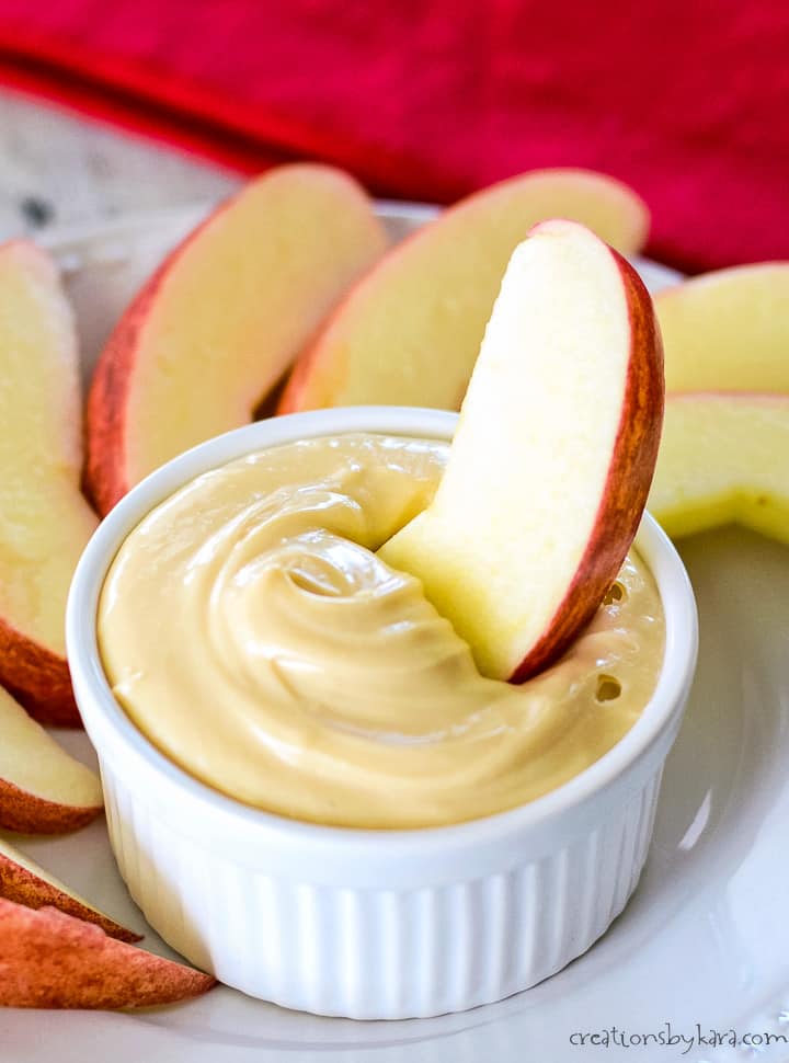 slice of apple being dipped in a bowl of caramel cream cheese apple dip