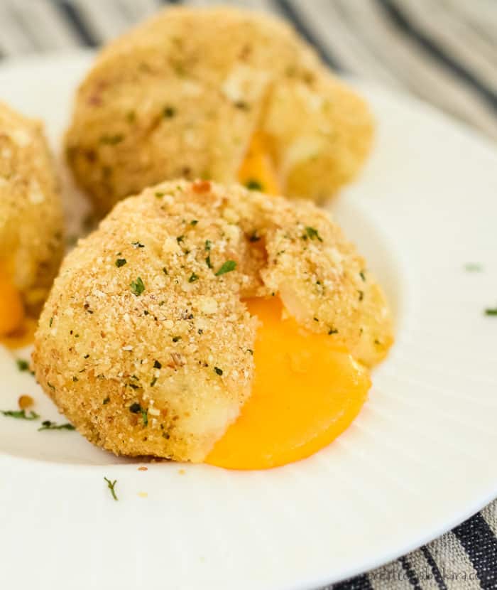 crunchy baked mashed potato balls on a plate, one with the melted cheese oozing out.