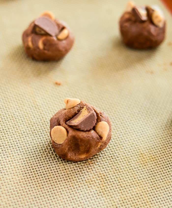 baking sheet of chocolate cookie dough balls with peanut butter chips pressed on the top