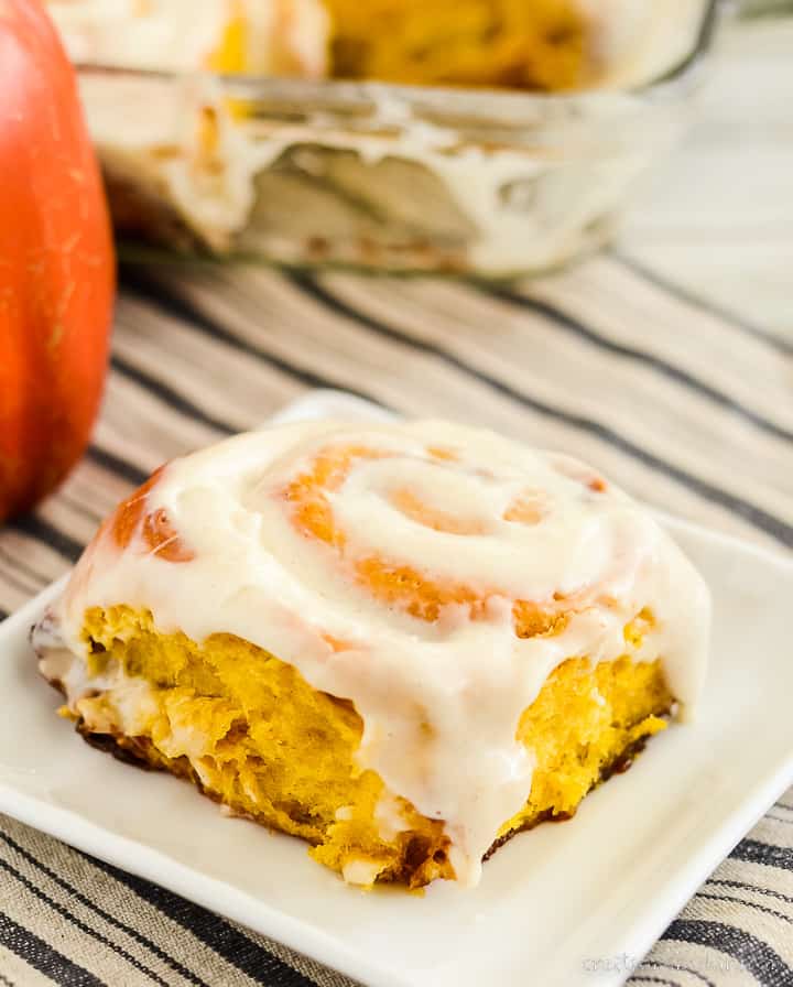 pumpkin spice cinnamon roll on a plate with a pan of rolls in the background