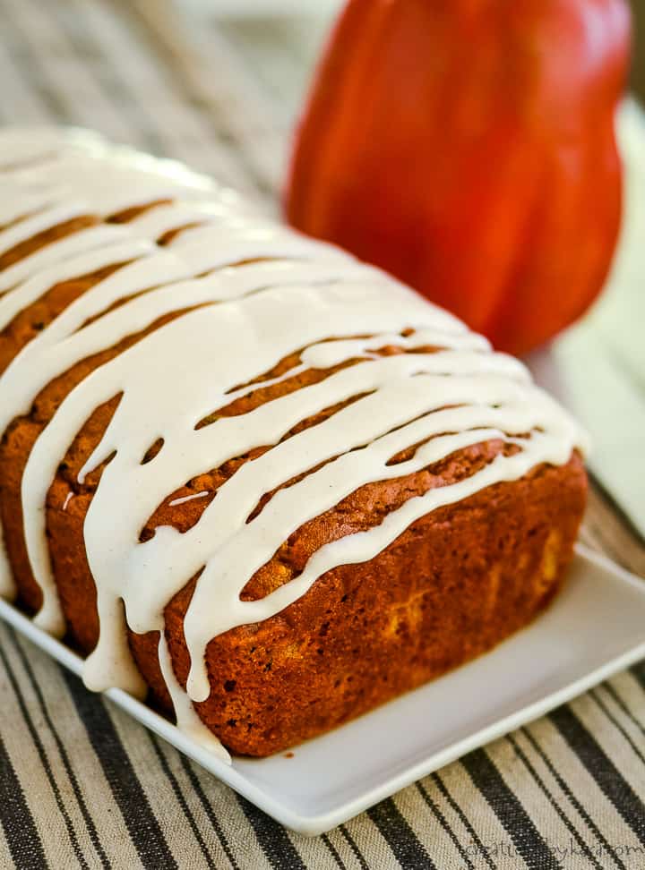 loaf of glazed pumpkin zucchini bread on a white tray with a pumpkin in the background.