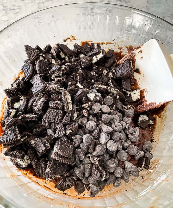 adding chocolate chips and oreo chunks to brownie batter