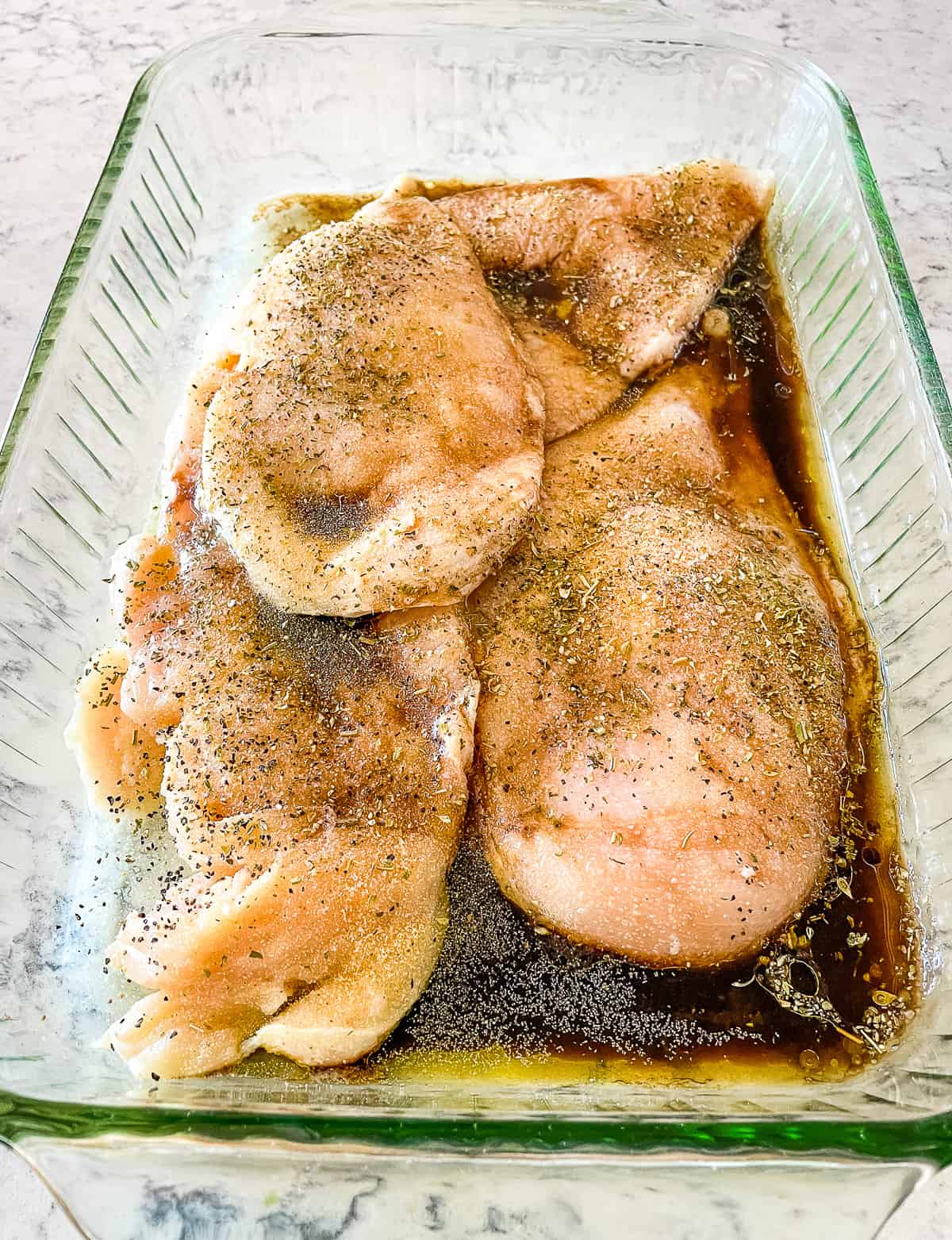 chicken breast marinating in a glass baking dish