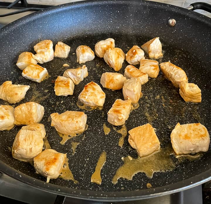 chunks of chicken being browned in a skillet