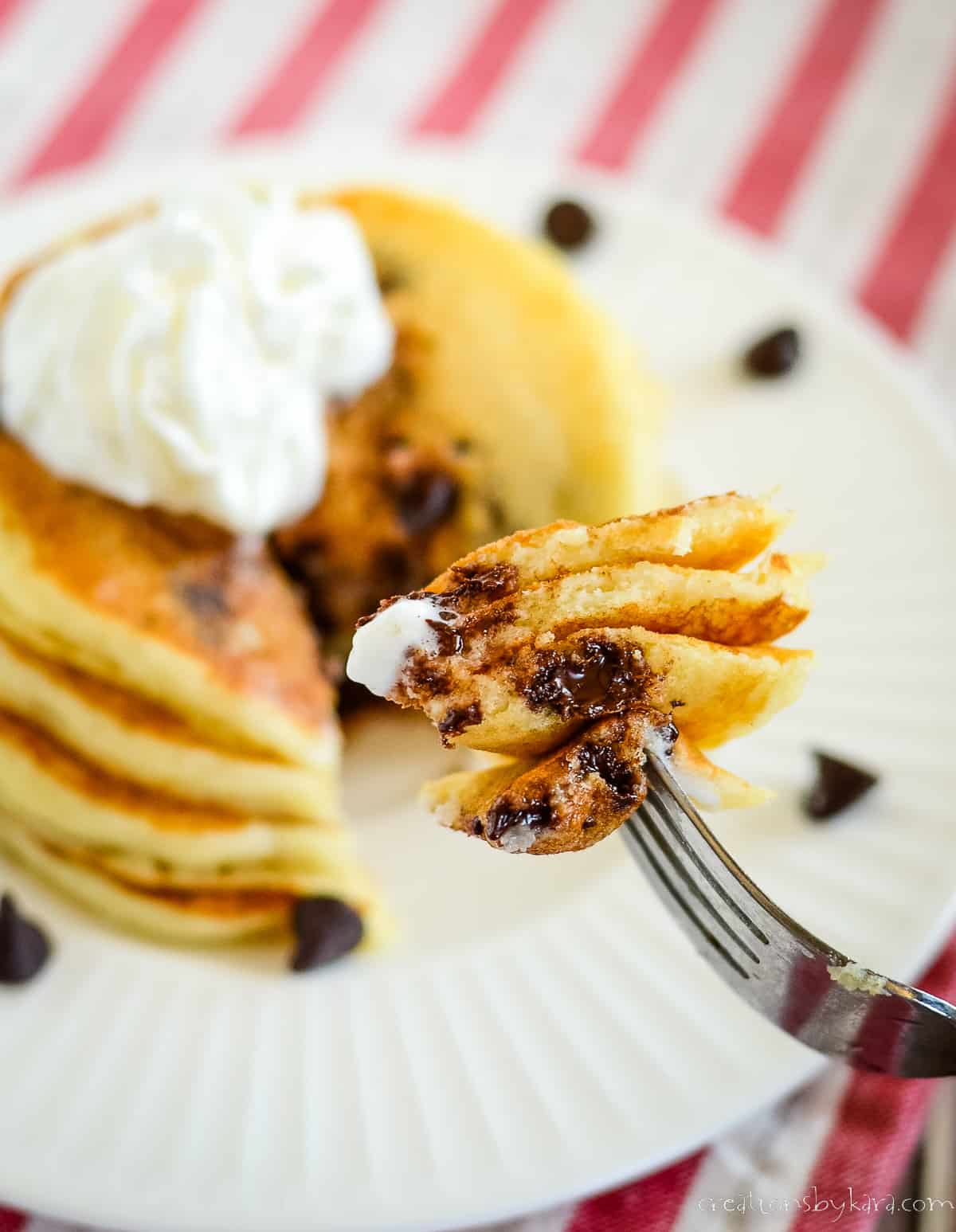 fork with chocolate chip pancakes and a plate of pancakes in the background