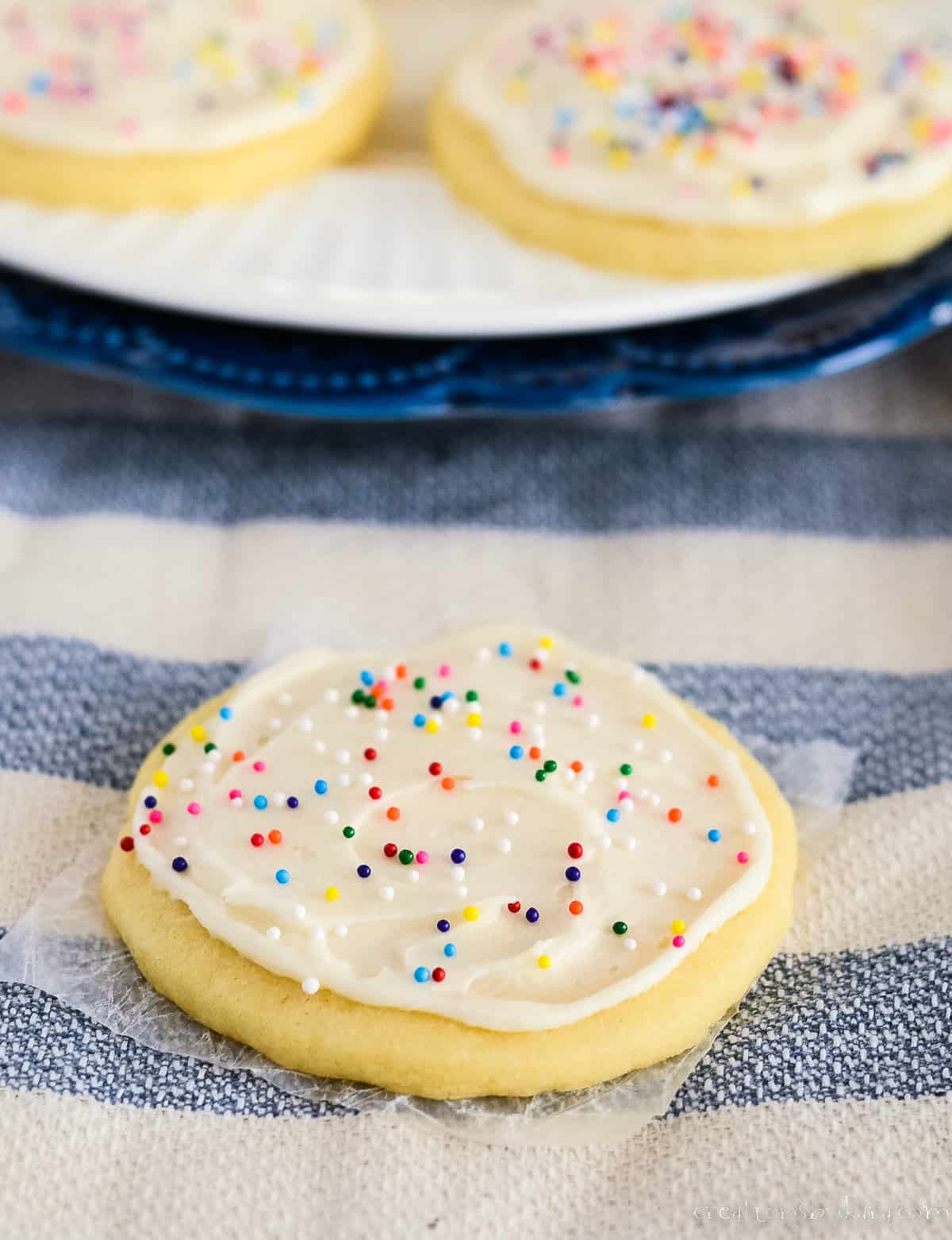 frosted sugar cookie on waxed paper with a plate of cookies in the background