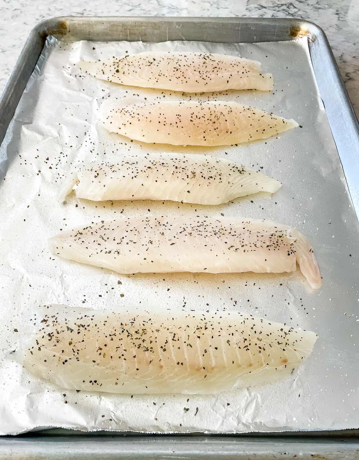 uncooked tilapia on a foil lined baking sheet