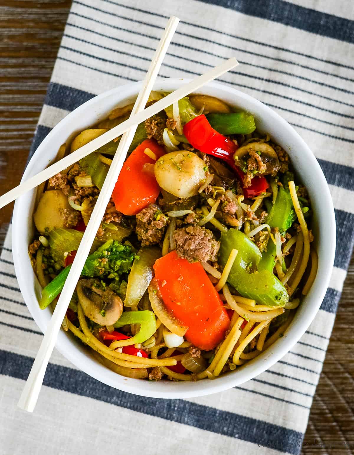 overhead shot of bowl of beef and broccoli lo mein with chopsticks sitting on the bowl.