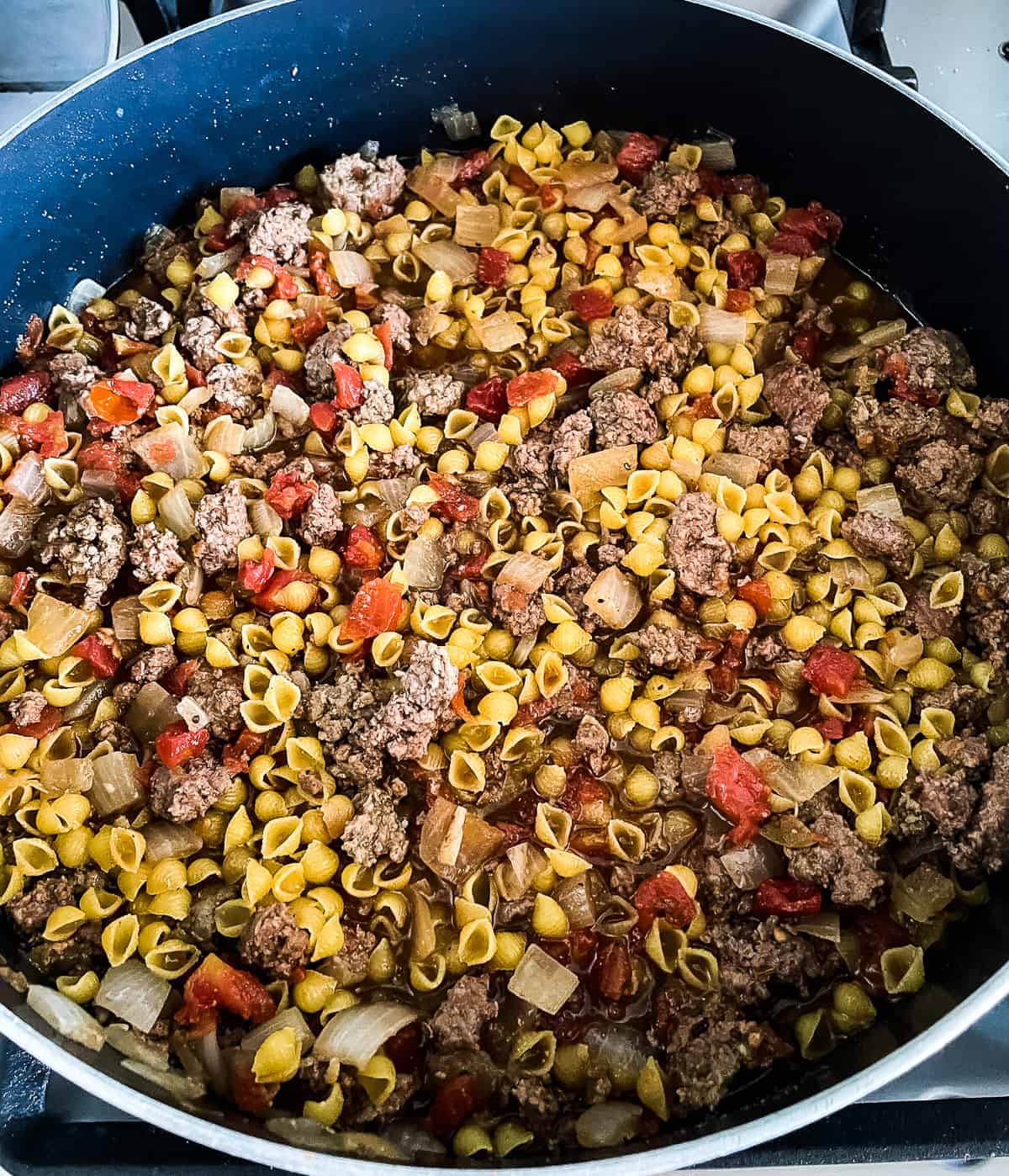 process shot- beef, pasta, tomatoes, onions, and spices cooking in a skillet