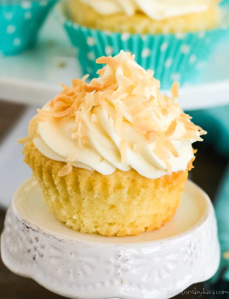 unwrapped cupcake with cream cheese frosting and toasted coconut on a white cupcake stand