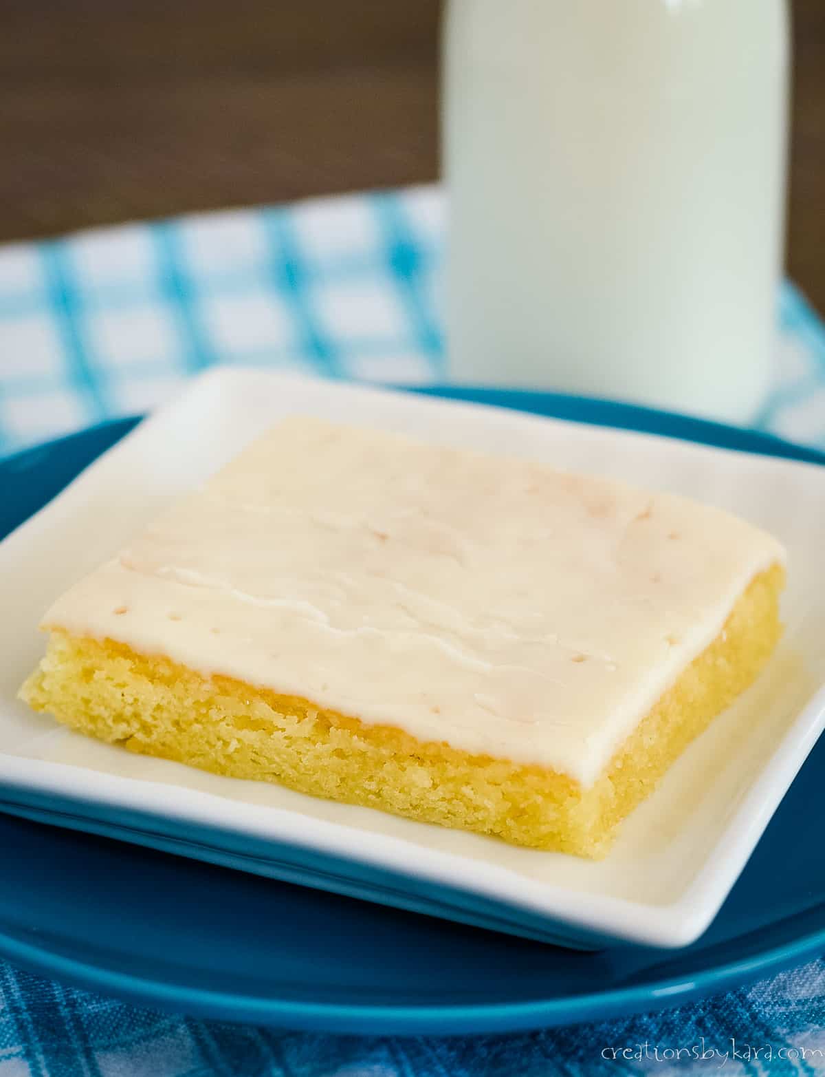 plate of white texas sheet cake with almond frosting, a glass of milk in the background