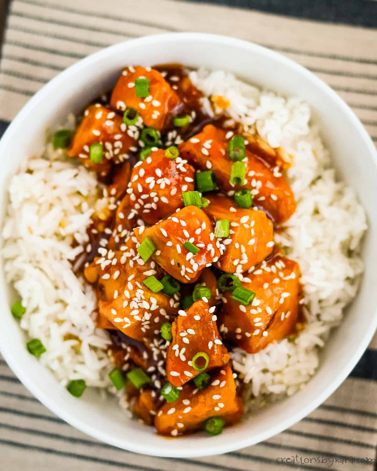 bowl of honey garlic chicken sprinkled with green onions and sesame seeds