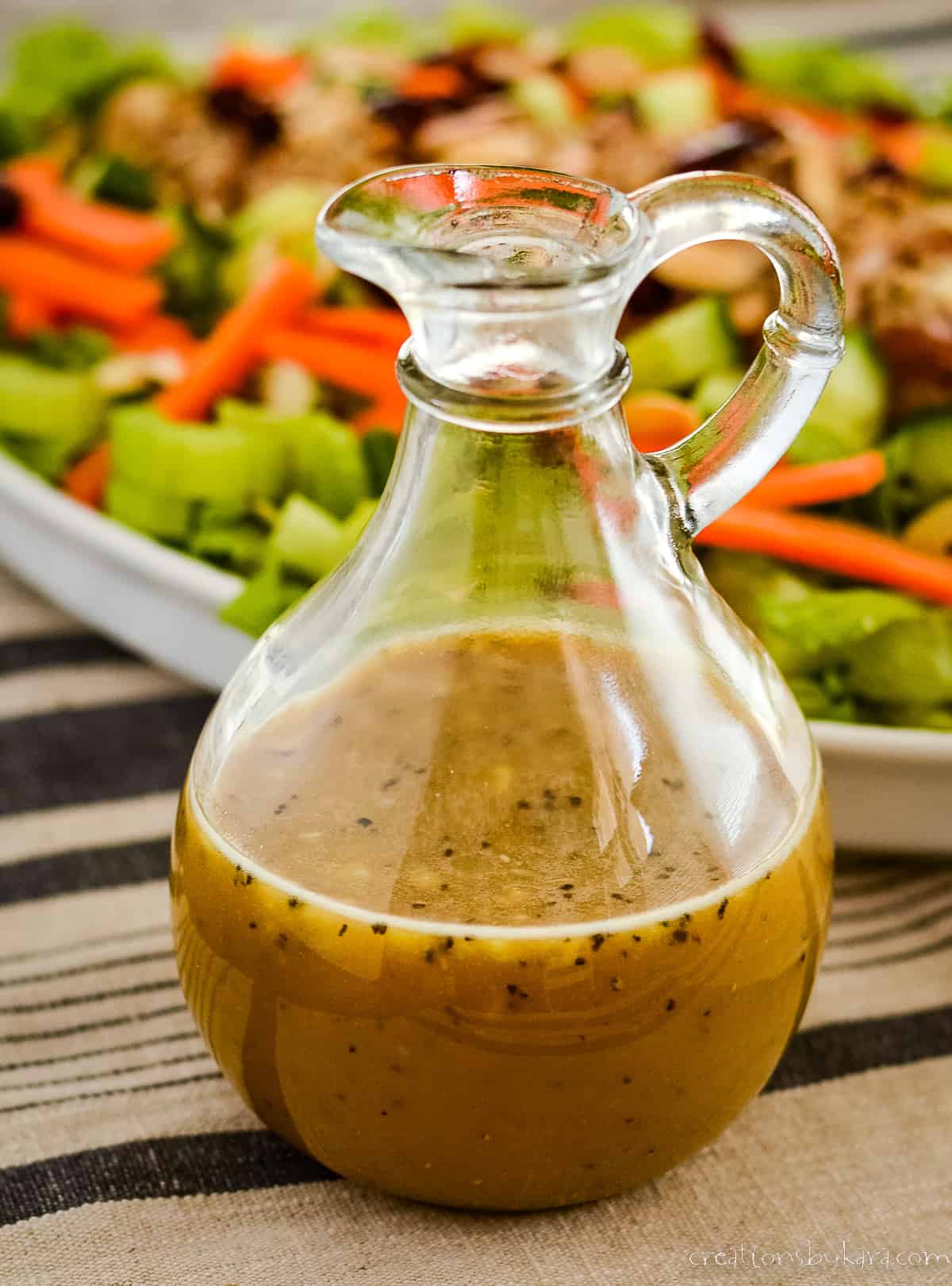 bottle of homemade honey mustard dressing in front of a plate of salad