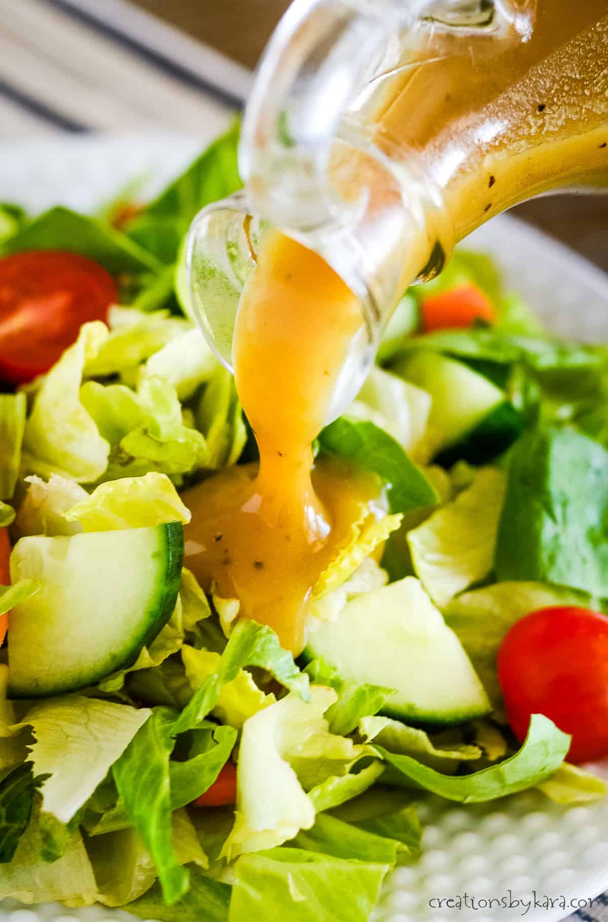 honey mustard dressing being poured on a plate of green salad