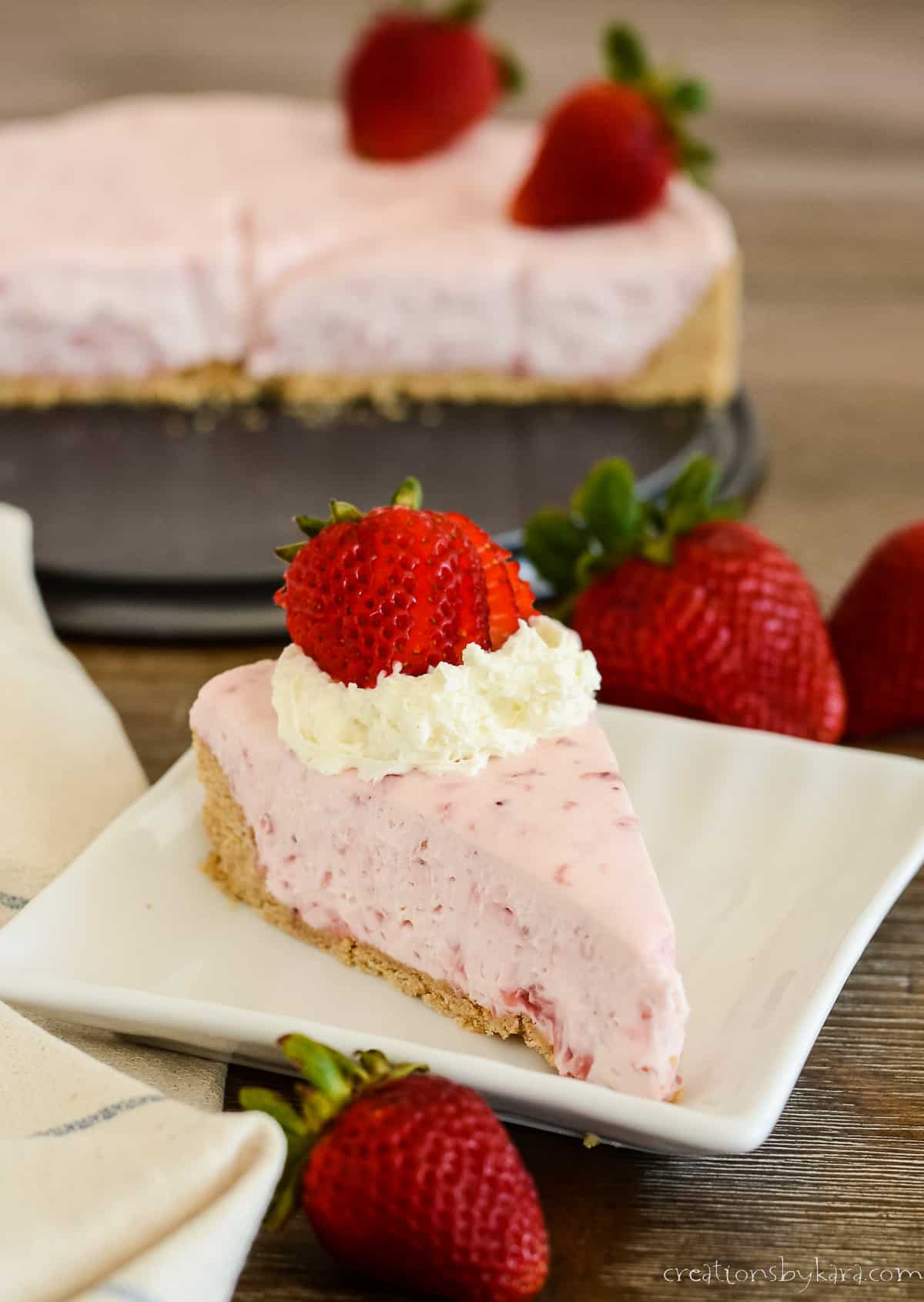no bake strawberry cheesecake on a plate with a whole cheesecake in the background